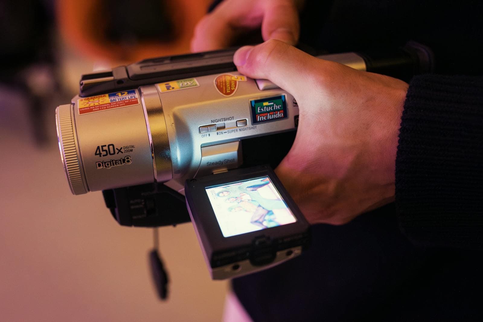 Hand operating a vintage digital camcorder with the LCD screen flipped out