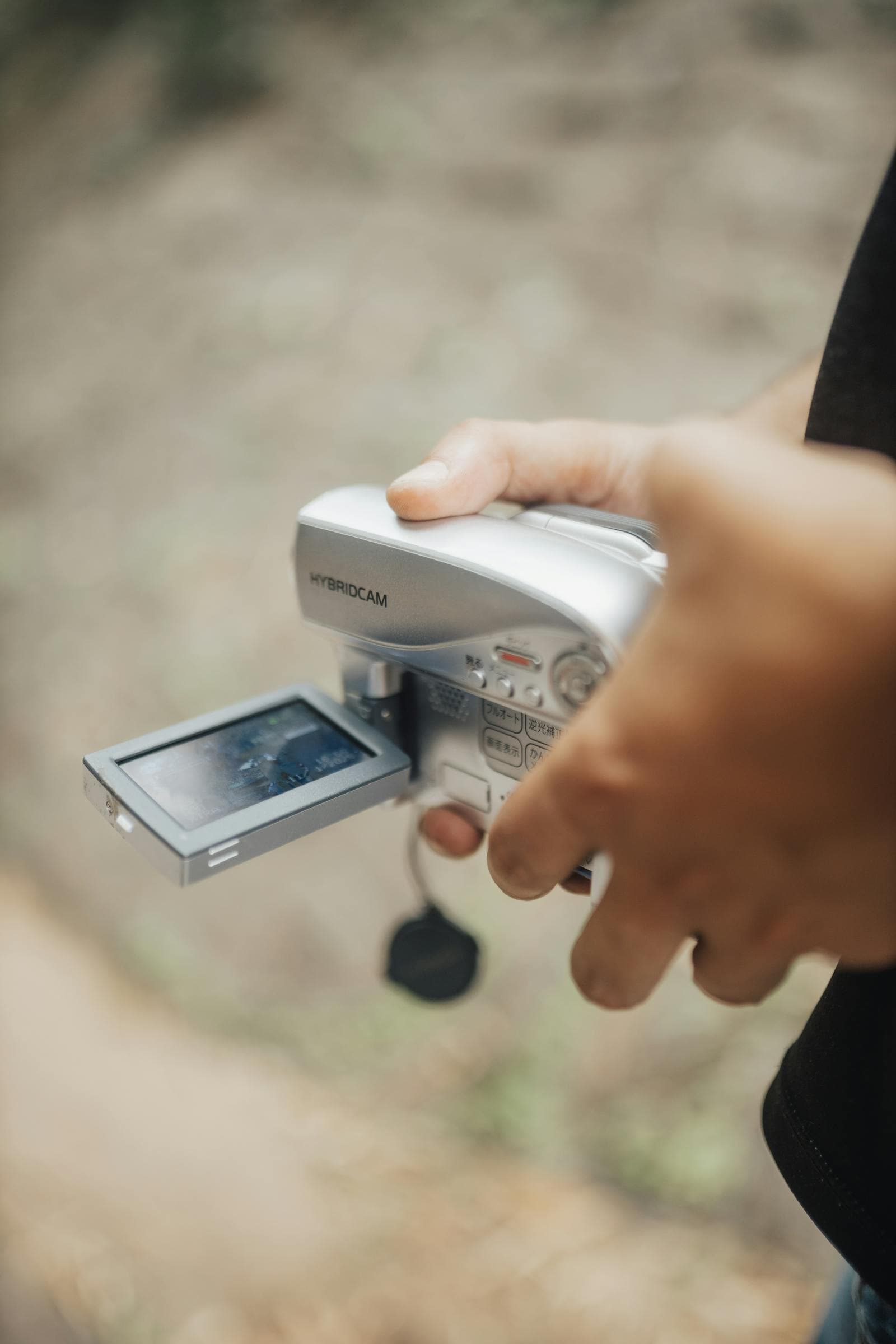 Person holding a vintage camcorder outdoors with its flip-out LCD screen open
